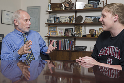 Charles Bierbauer sitting at a long wooden table having an animated conversation with a student