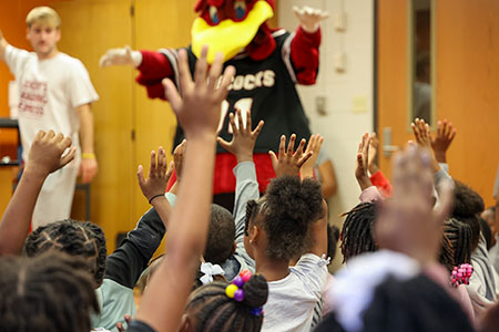 USC mascot Cocky standing in front of a classroom of students with their hands raised