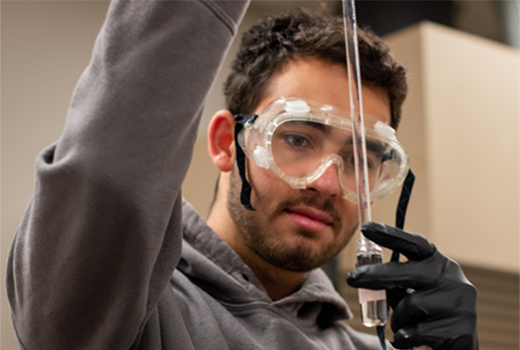 Student wearing safety goggles holding long dropper tube and small test tube.