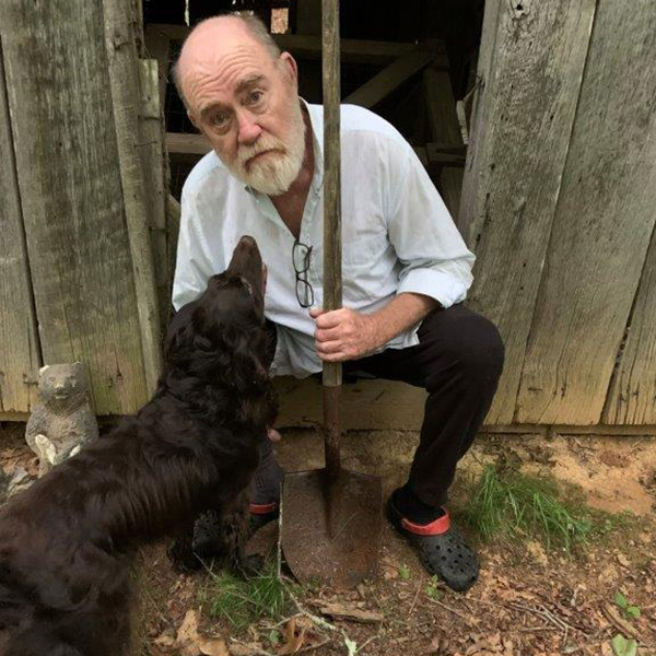 Dr Wally Peters holding a shovel and kneeling with his dog