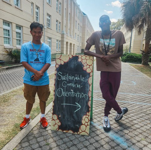 Two students standing beside a sign reading 'Sustainable Carolina Orientation'